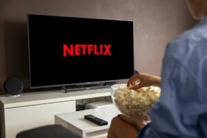 uomo guarda in tv netflix con scodella di pop corn in mano