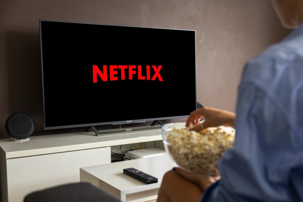 uomo guarda in tv netflix con scodella di pop corn in mano